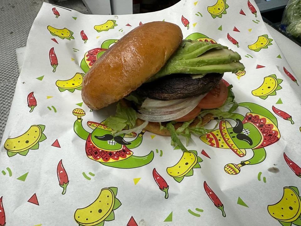 A burger on a toasted bun with sliced avocado, lettuce, tomato and onion