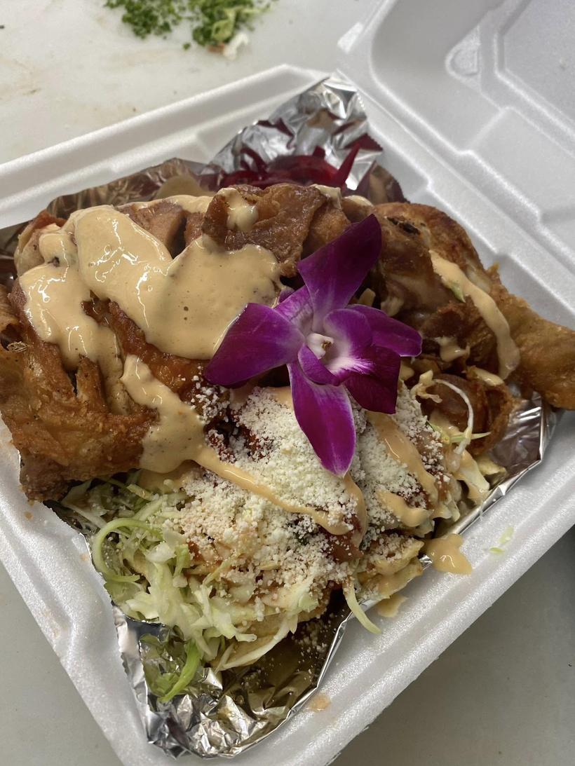 A takeout container of crispy fried pieces topped with crema and crumbled cheese
