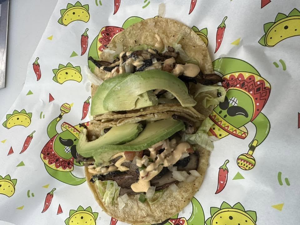 Two tacos topped with sliced avocado, lettuce and chipotle sauce