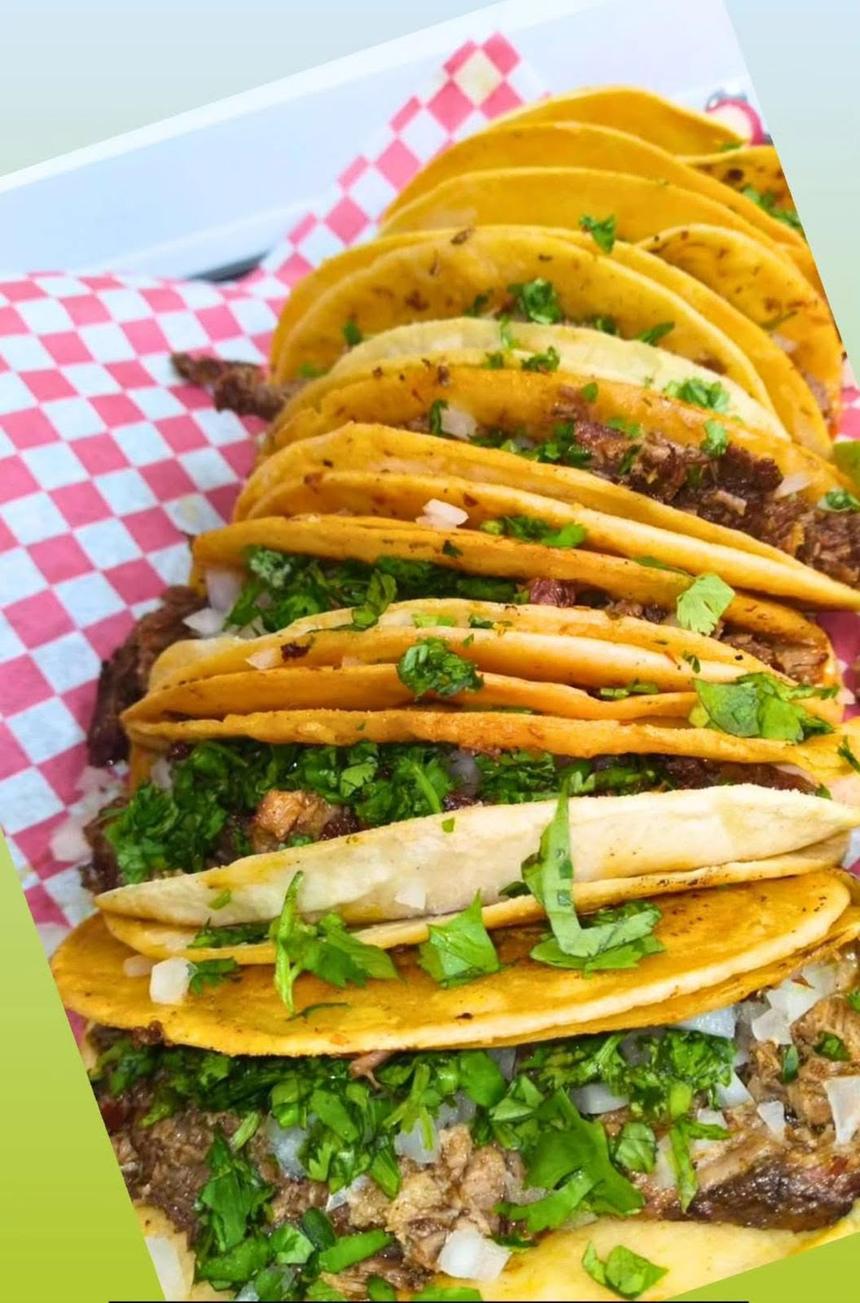 A row of street tacos topped with chopped onions and cilantro